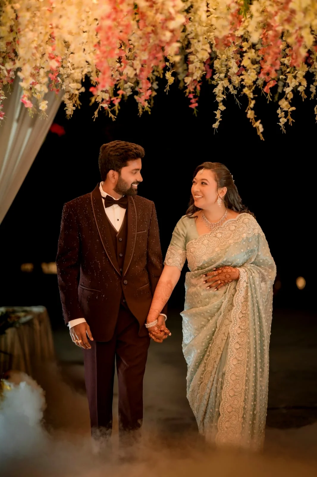 Wedding couple walking together beneath a floral installation